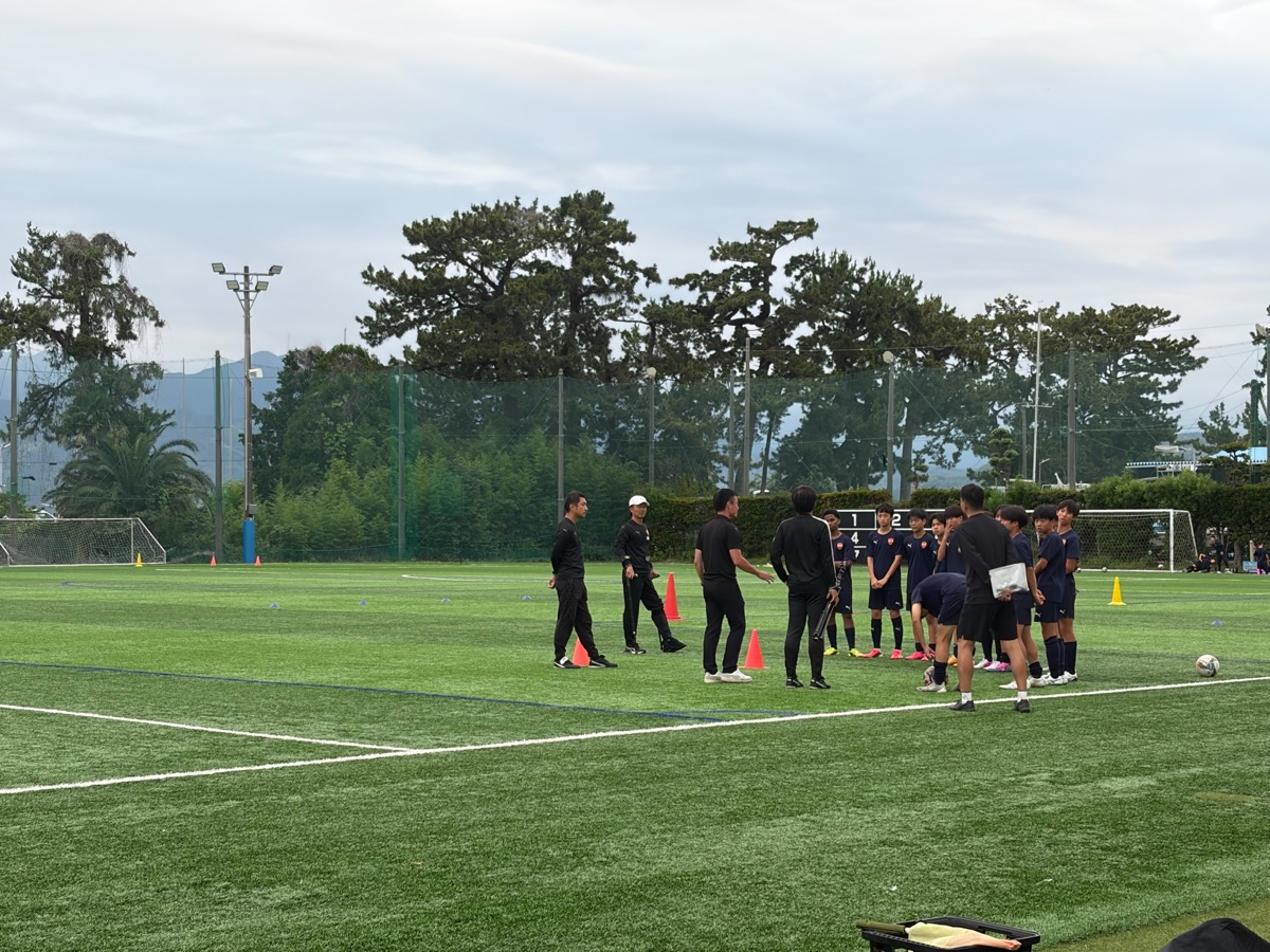 Coaches briefing youth players on the pitch during a Japan football tour